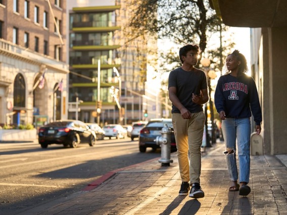 2 students walk on a sidewalk in downtown Tucson