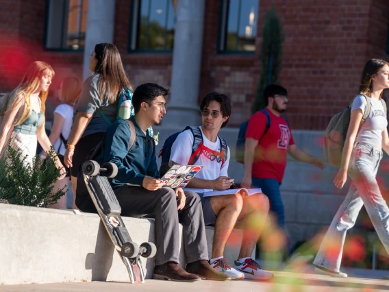 Students sitting outside on a concrete wall with laptop and books.