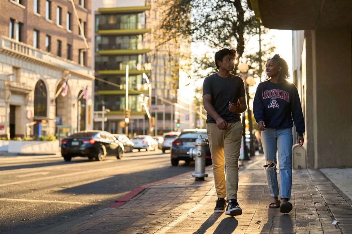 2 students walk on a sidewalk in downtown Tucson