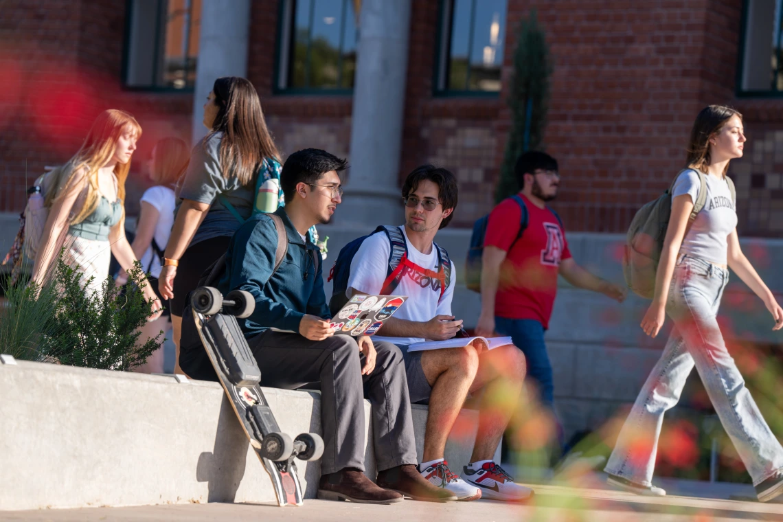 Students sitting outside on a concrete wall with laptop and books.