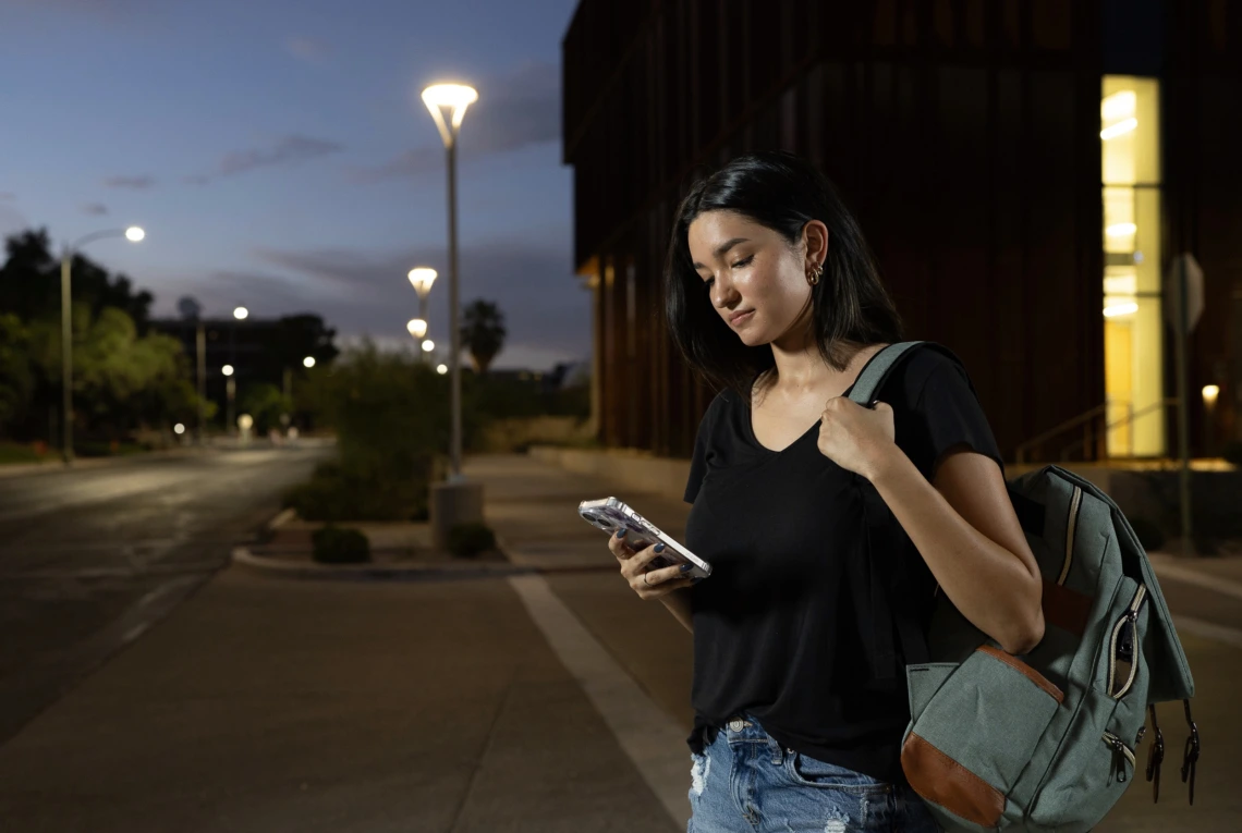 Famale college student at night walking alone on campus looking at her phone and SafeCats app.