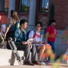 Students sitting outside on a concrete wall with laptop and books.